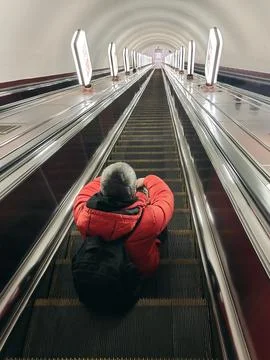 A man with a backpack sits on the steps of the escalator and goes down Stock Photos