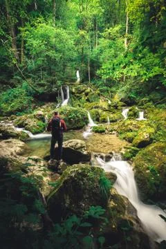 Man with backpack sits on stone at a waterfall in the forest and meditates al Stock Photos