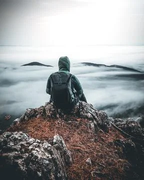 Man with Backpack sitting alone on Mountain Peak over a sea of clouds in austria Stock Photos