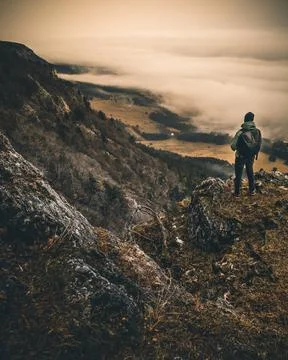 Man with Backpack sitting alone on Mountain Peak over a sea of clouds in austria Stock Photos