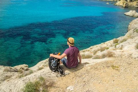 Man with backpack sitting on cliff above sea Stock Photos