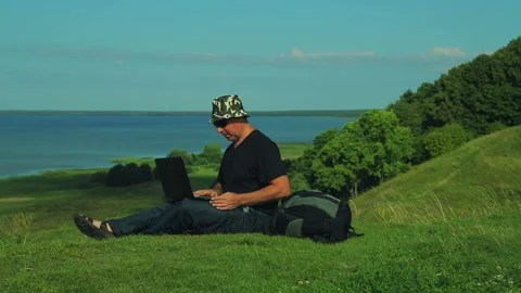 Man with a backpack sitting at the edge of the mountain overlooking the lake and Stock Footage 96080403