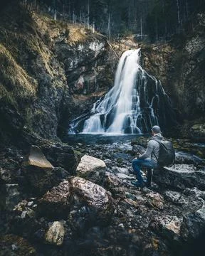 Man with backpack sitting in front of waterfall Stock Photos