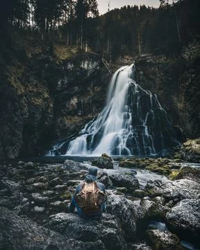 Man with backpack sitting in front of waterfall Stock Photos