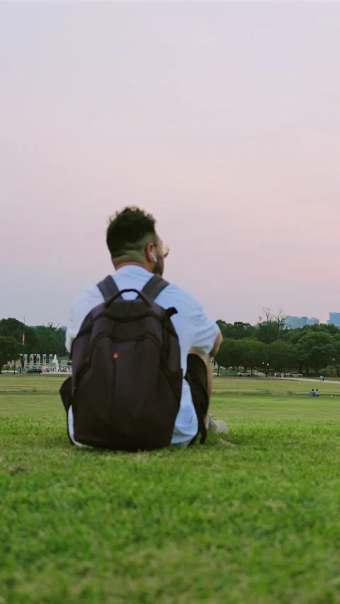 Man with Backpack Sitting on Green Lawn at Sunset in Washington DC. Vídeo Stock 342959044