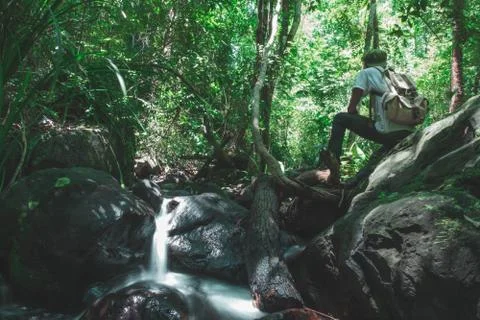 A man with a backpack sitting on rock in the stream looking at the greatness Stock Photos