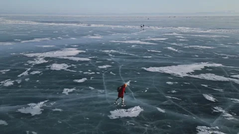 Man with a backpack is skating on the blue transparent ice of the lake Baikal Stock Footage 278020343