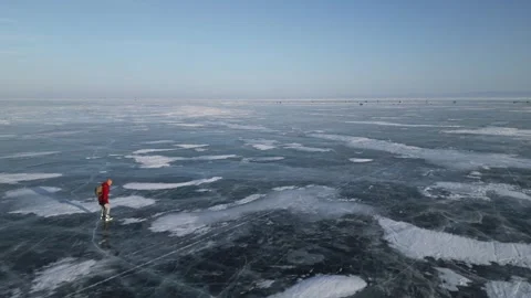Man with a backpack is skating on the blue transparent ice of the lake Baikal Stock Footage 278020402