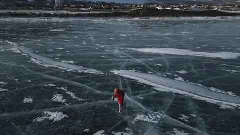 Man with a backpack is skating on the blue transparent ice of the lake Baikal Stock Footage 278020470