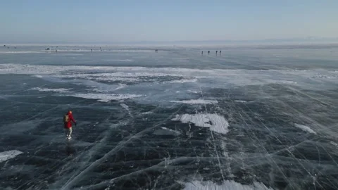 Man with a backpack is skating on the blue transparent ice of the lake Baikal Stock Footage 278020556