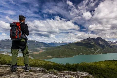 Man with backpack standing on the cliff in mountains at above lake Stock Photos