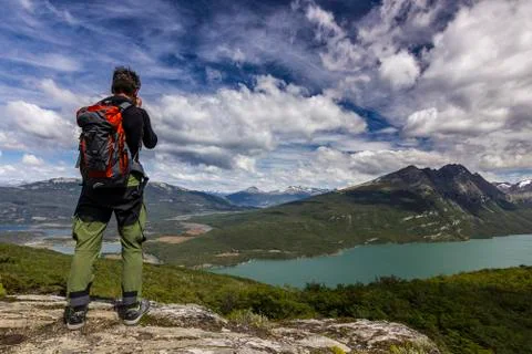 Man with backpack standing on the cliff in mountains at above lake Stock Photos