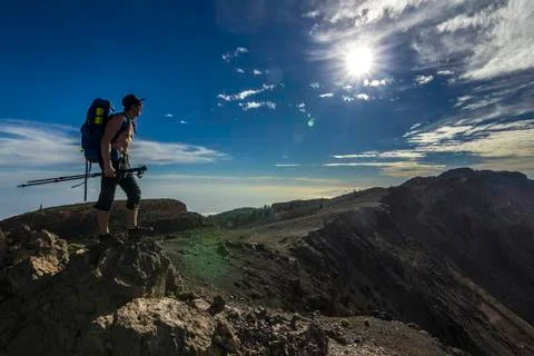 Man with backpack standing on a cliff in mountains with blue sky and sun Stock Photos