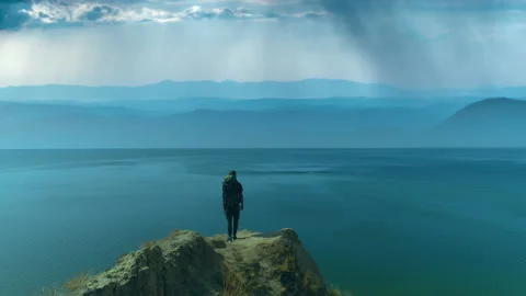 The man with backpack standing on the mountain edge on the seascape background Stock Footage 143033098