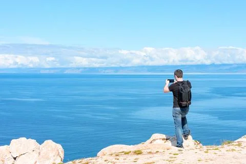 Man with backpack standing on a rock at the end of earth using his smartphone Stock Photos