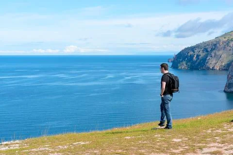 Man with backpack standing on a rock at the end of earth watching on the bright Stock Photos
