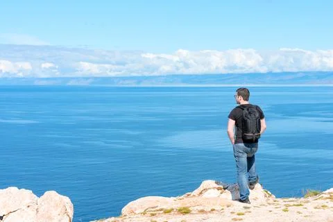 Man with backpack standing on a rock at the end of earth watching on the bright 库存照片