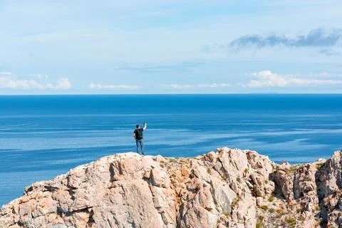 Man with backpack standing on a rock at the end of earth using his smartphone Stock Photos