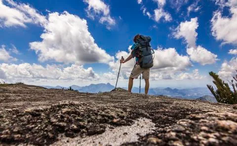 Man with backpack standing on top of mountain with blue sky with clouds Stock Photos