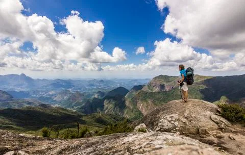 Man with backpack standing on top of mountain with blue sky with clouds Stock Photos