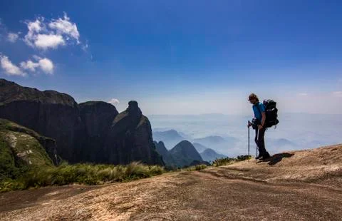 Man with backpack standing on top of mountain with blue sky with clouds Stock Photos