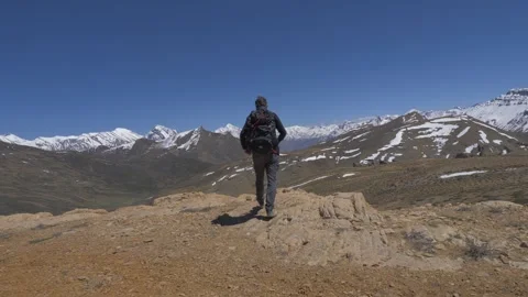 A man with a backpack stands against the background of snowy mountains Stock Footage 141792170
