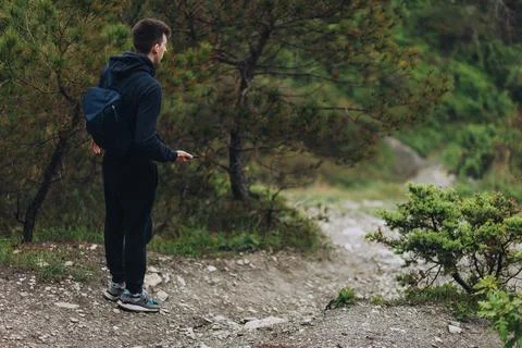 A man with backpack stands in the beginning of trail road in mountains. Young Stock Photos