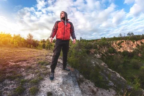 A man with a backpack stands on the edge of a cliff and looks at the sunset Stock Photos