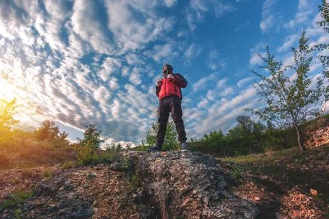 A man with a backpack stands on the edge of a cliff and looks at the sunset Stock Photos