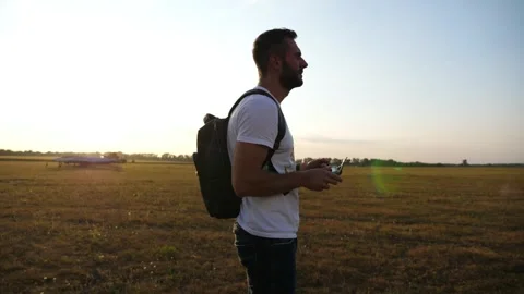 Man with backpack stands in open field, preparing to launch drone, showcasing Видео 347872101