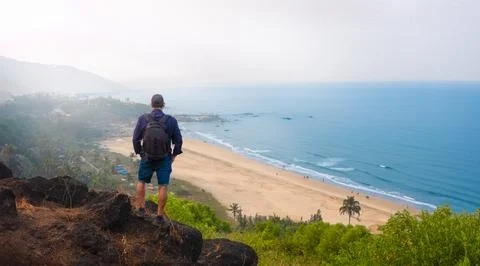 Man with backpack stands on a rock looking at the sea Goa India Stock Photos