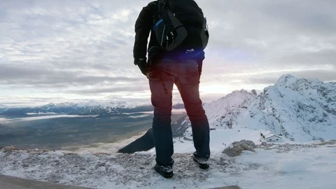 Man with backpack stands on top of mountain looking a sunset in the horizon Stock Footage 100052621