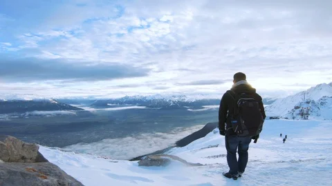 Man with backpack stands on top of mountain looking a sunset in the horizon Stock Footage 100052928