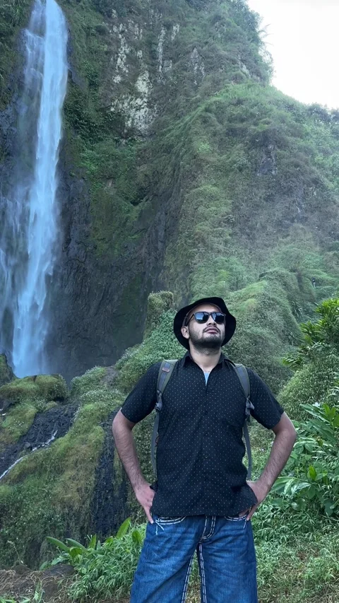 Man with Backpack by Tall Waterfall in Green Forest Vertical Shot Stock Footage 323908264