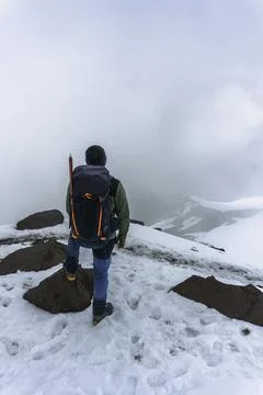 Man with backpack trekking in mountains. Cold weather, snow on hills. Stock Photos