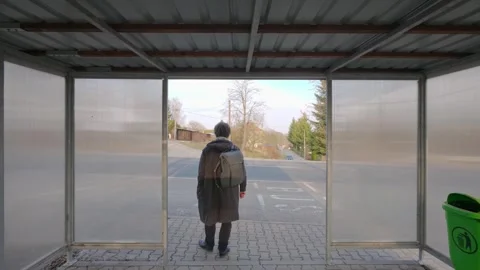 Man with backpack waiting at bus stop, looking around. Urban scene capturing Stock Footage 333286865