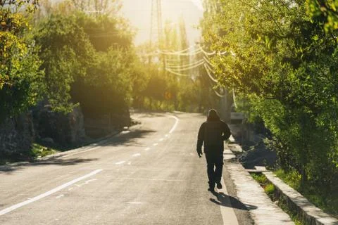 A man with backpack walking alone on empty road in the morning Stock Photos