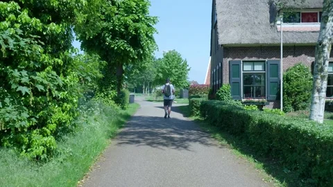 Man with backpack walking along a country road in a dutch village Stockbeeldmateriaal 336903168