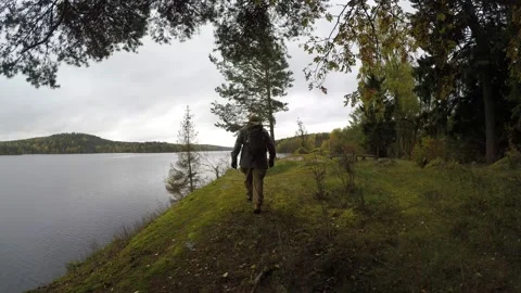 Man with backpack walking along remote lakeside Stock Footage 145342692