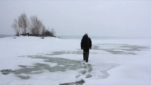 Man with a backpack walking in a blizzard on a melting river surface Stock Footage 87823649