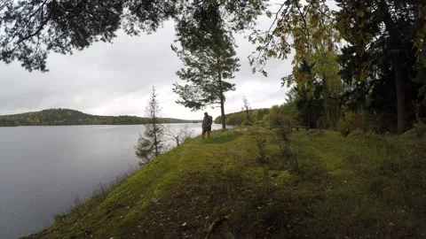 Man with backpack walking towards camera along remote lakeside Stock Footage 145342696