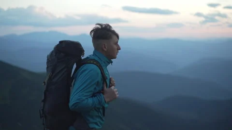 A man with a backpack walks against the wind against the background of mountains Stock Footage 240550202