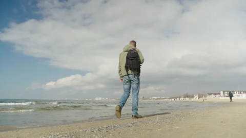 A man with a backpack walks along the sandy beach on a sunny day. A traveler Video stock 172035356