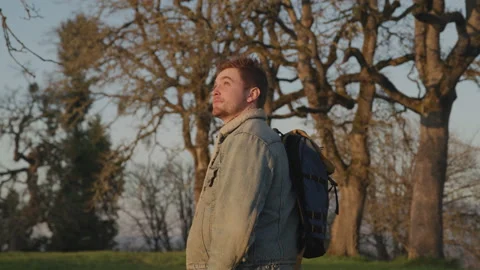 Man with a Backpack Walks up a Grassy Hill and Turns to Look at the Sky Stock Footage 210218023