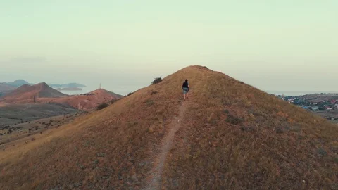A man with a backpack walks the hills against the backdrop of a valley with Stock Footage 95168166