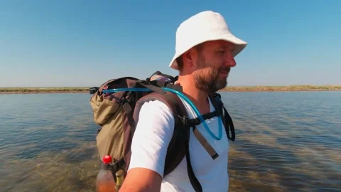 A man with a backpack walks knee-deep in water through the estuary on a sum.. Stock Footage 272781559