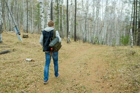 A man with a backpack walks through the forest in spring. Yellow withered lea Stock Photos