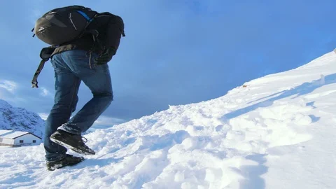 Man with backpack walks towards the top of a snow covered mountain Stock Footage 100052982