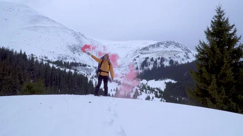 A man with a backpack waving pink smoke bomb in the mountains in winter Stock Footage 129596895