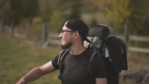 Man backpacker walking in glasses raises hand to cover eyes to look at mountains Stock Footage 139053946